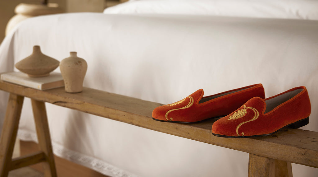 Orange slippers on a wooden bench with a bed in the background