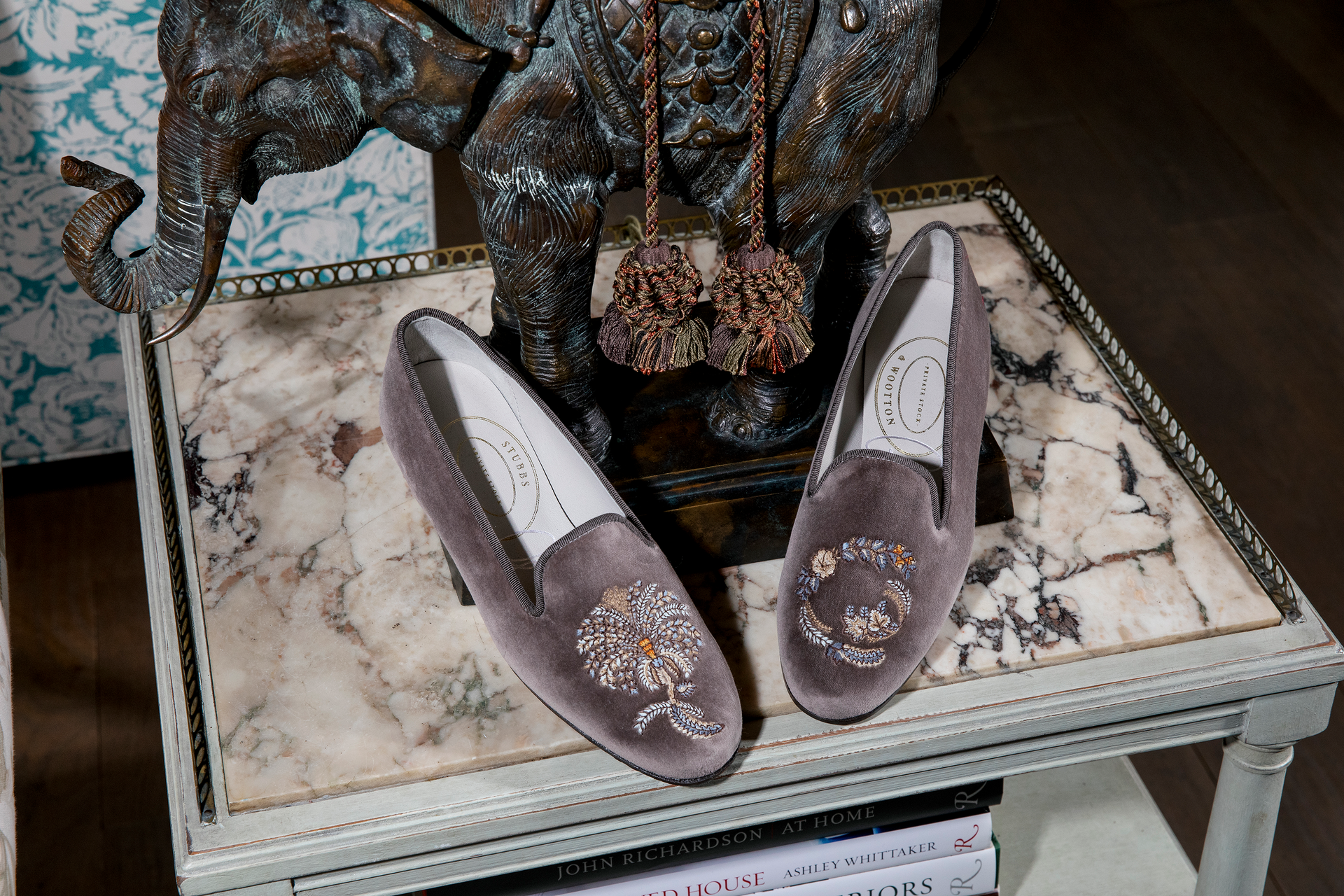 Grey slippers with floral embroidery resting on a marble table with a lamp