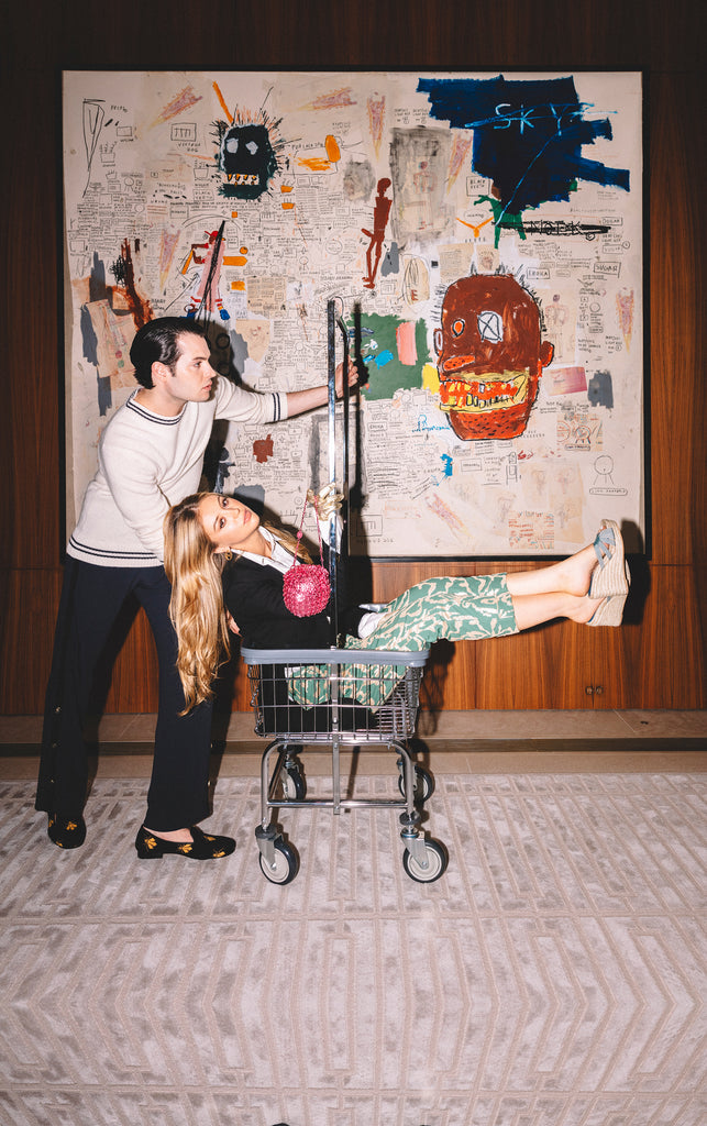 An image of a man and a woman standing in front of a Basquiat painting wearing luxury footwear.