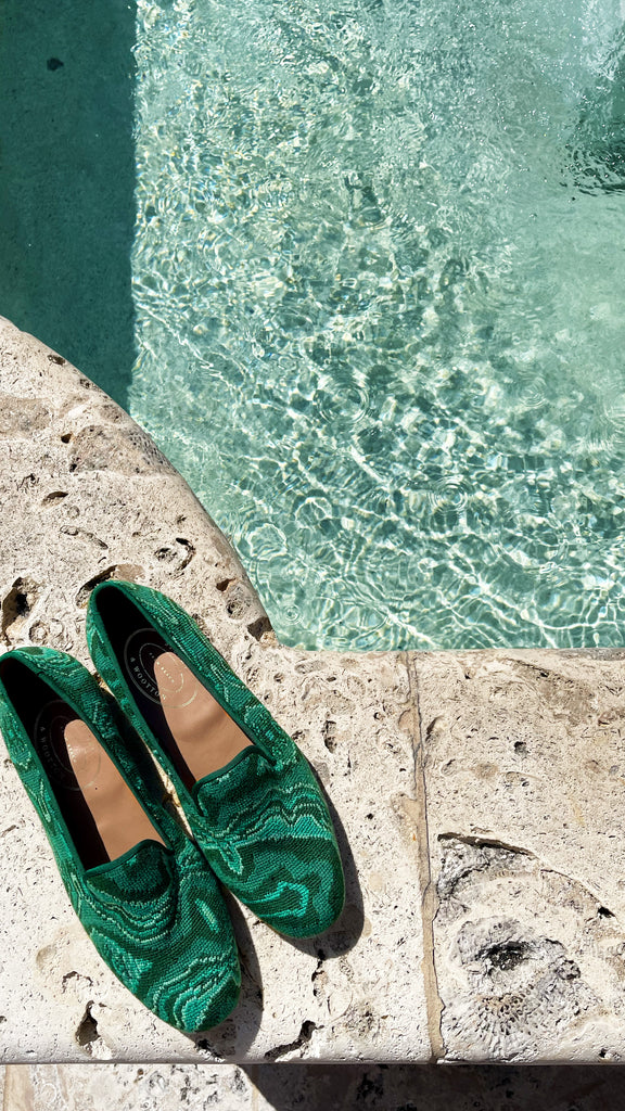 Two pairs of green slippers photographed beside a fountain.