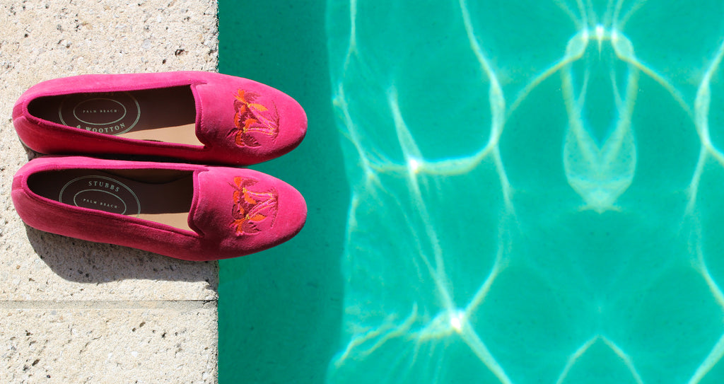 A pair of pink slippers resting on the edge of a stone pool deck.