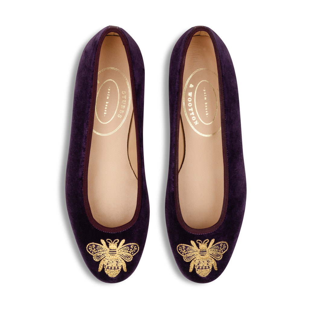 Pair of purple shoes with gold bee designs on a white background