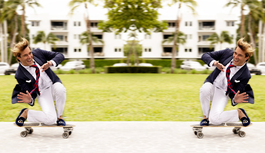 Reflected image of a man on skateboard wearing a white shirt, white pants, a tie, a blazer, and slippers.