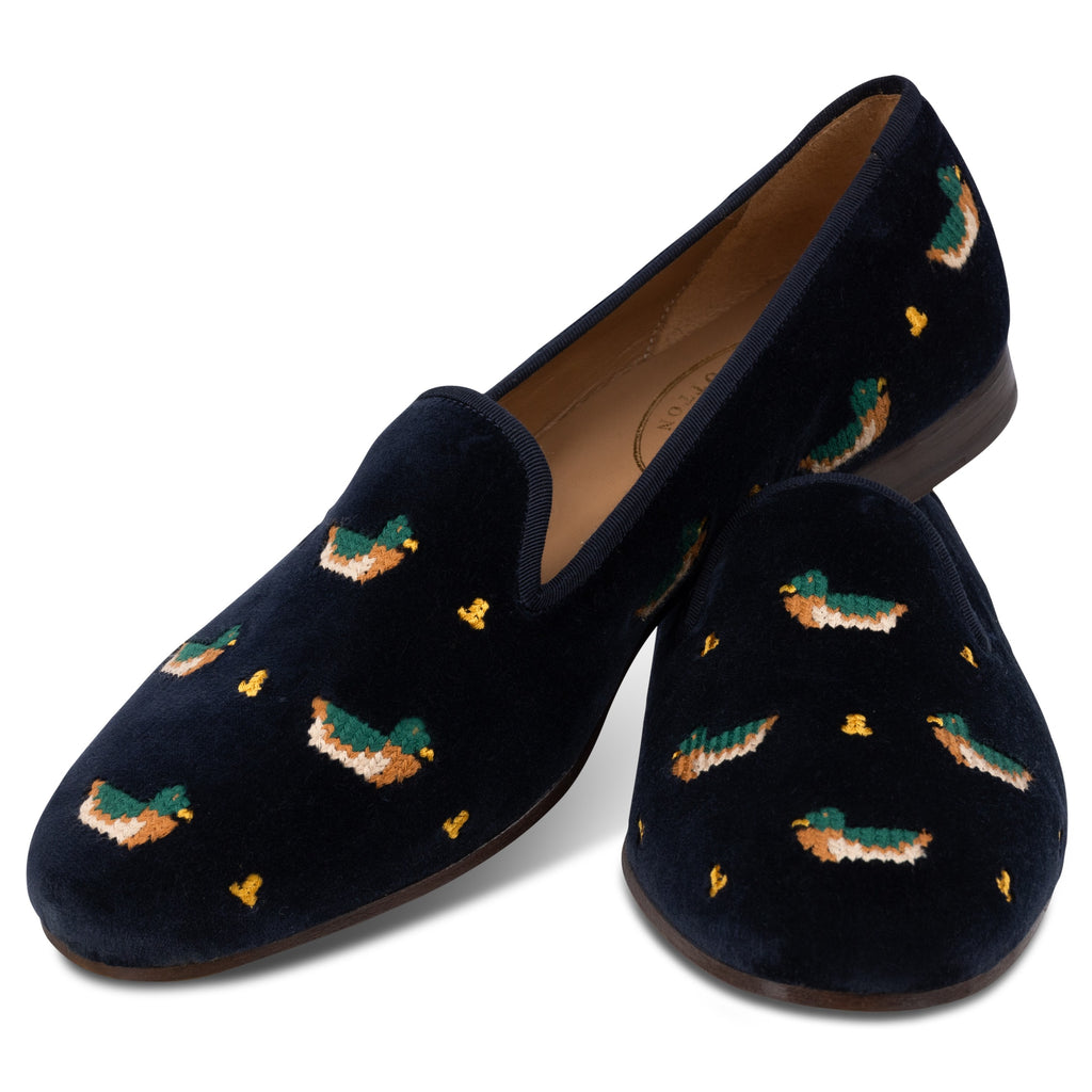 Navy velvet slippers with embroidered duck patterns on a white background