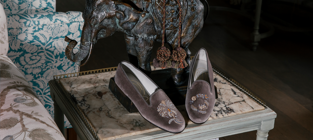 Grey slippers with floral embroidery resting on a marble table with a lamp