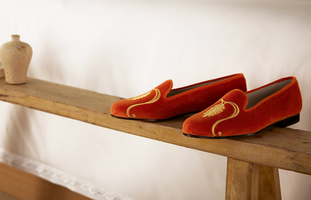 Pair of orange slippers sitting on a bench beside a bed.